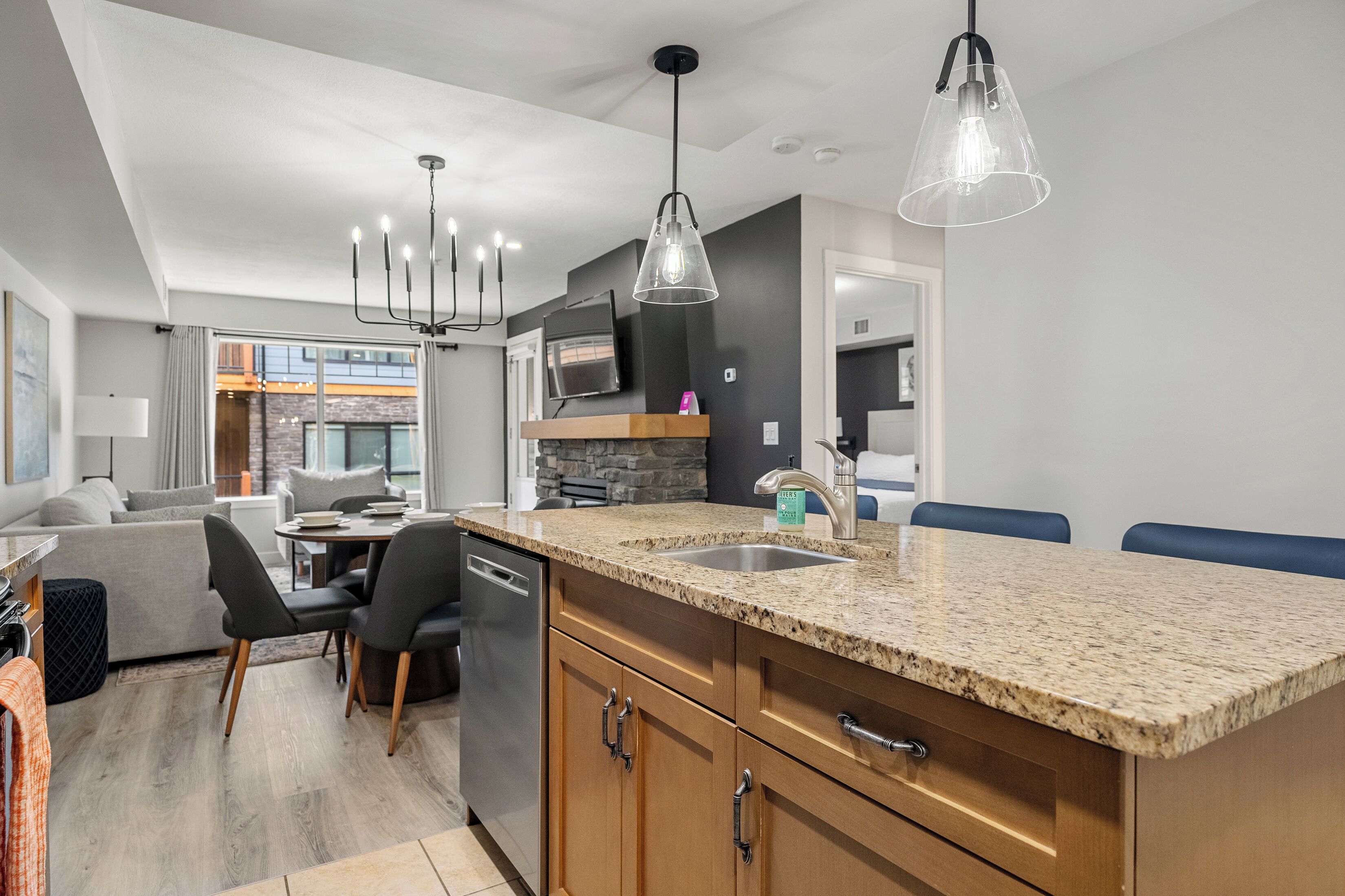 A modern kitchen with granite countertops, stainless steel appliances, and a dining area with a gray sofa and chairs.
