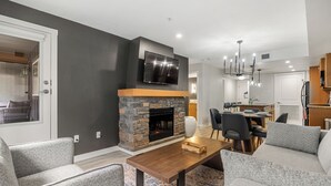 A modern living room with a stone fireplace, a flat-screen TV, and a dining area with a table and chairs. - Copperstone 2BR in the Canadian Rockies - Dog-Friendly, Shared Hot Tub (Dead Man's Flats)