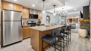 A modern kitchen with a stainless steel refrigerator, wooden cabinets, granite countertops, and a central island with bar stools. - Copperstone 2BR in the Canadian Rockies - Dog-Friendly, Shared Hot Tub (Dead Man's Flats)