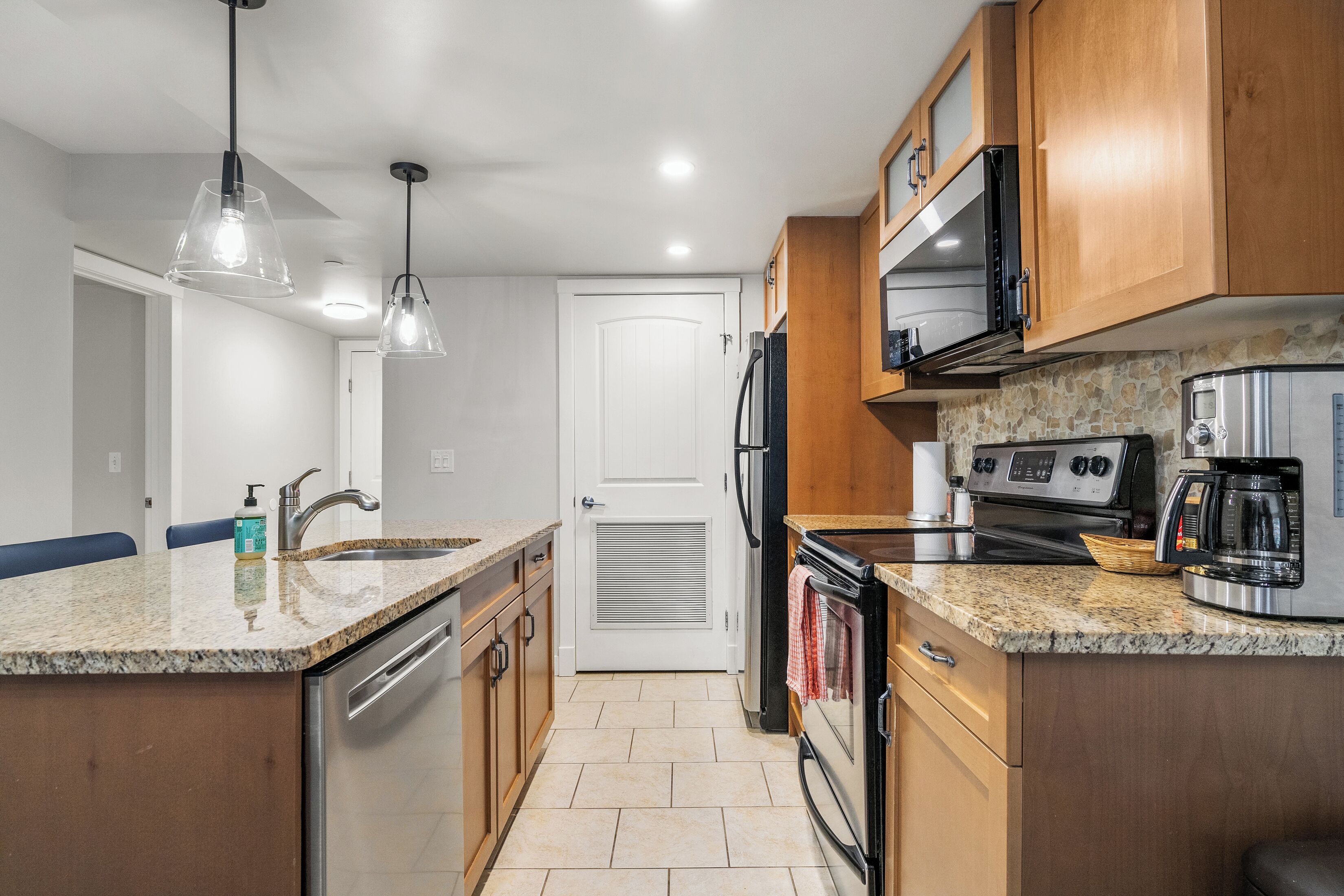 A kitchen with granite countertops, stainless steel appliances, wooden cabinets, and pendant lighting.