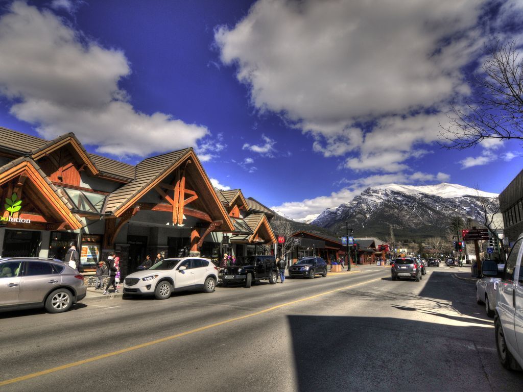 A street with wooden buildings, cars, and a mountain in the background.