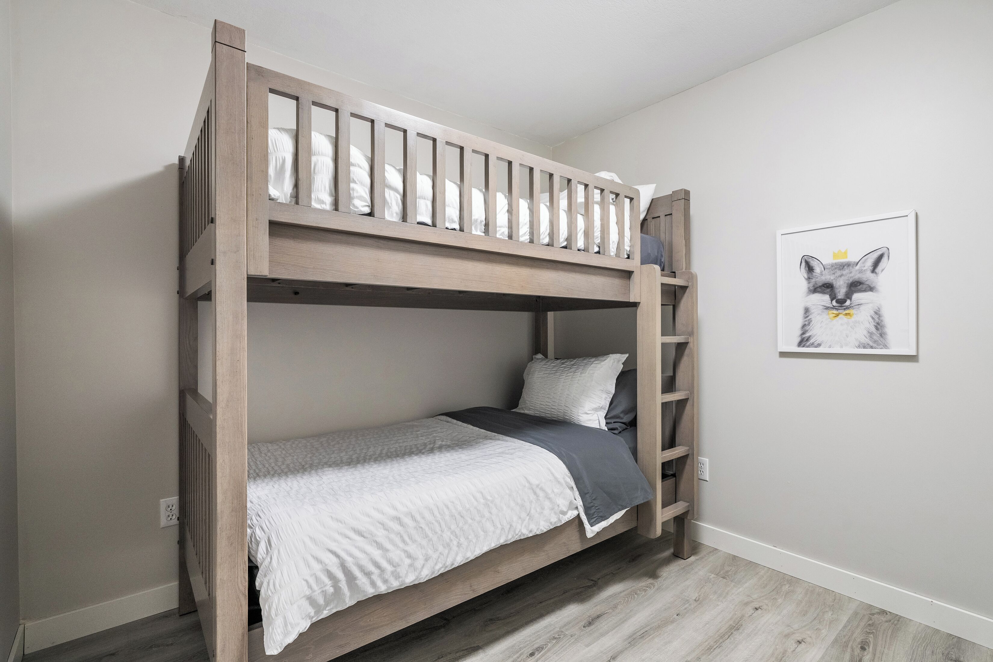 A bunk bed with a ladder, white bedding, and a framed picture of a fox on the wall.