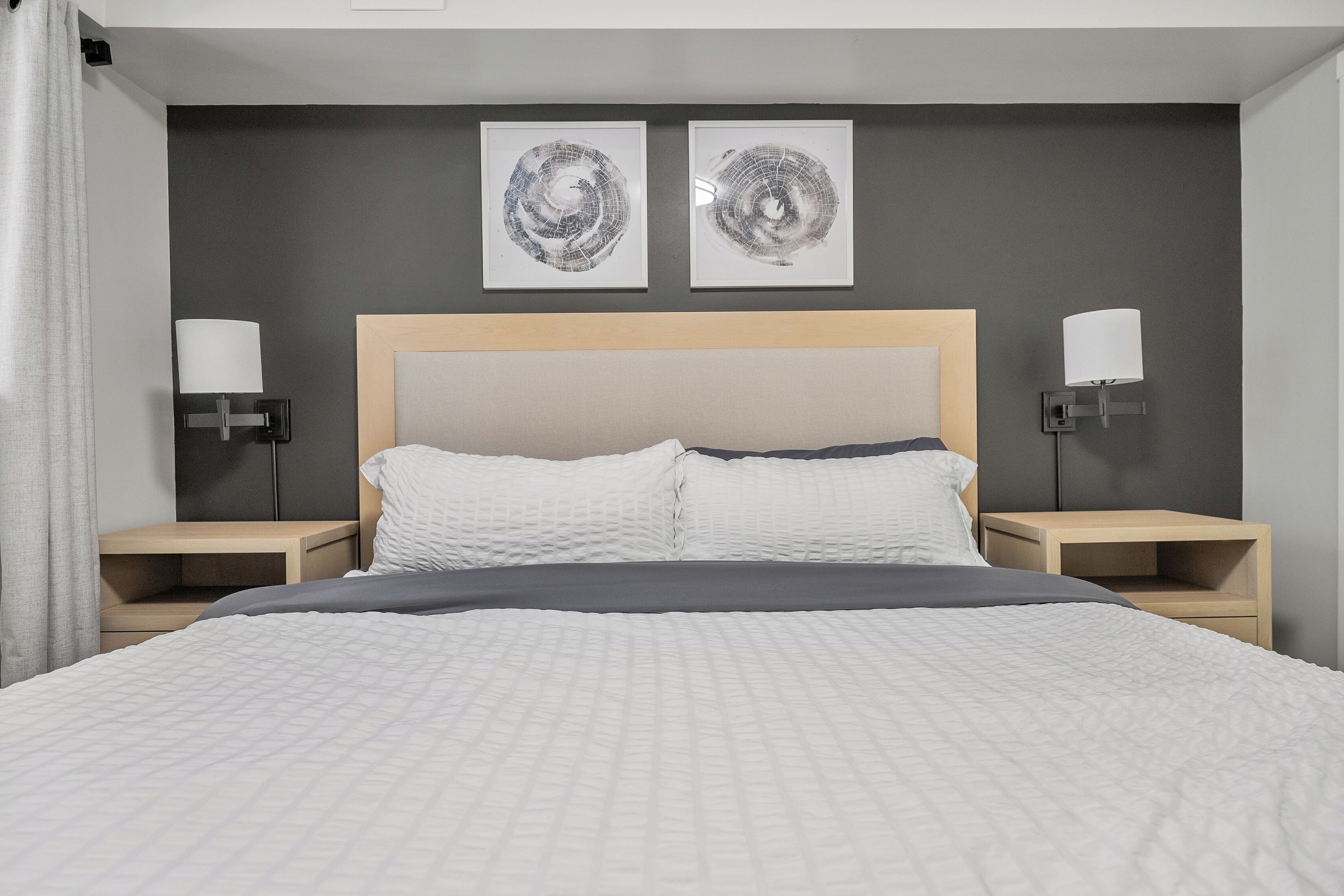 A modern hotel room with a large bed, two bedside tables, and two wall-mounted lamps.