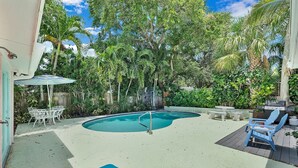 Un jardin avec une piscine, des chaises longues et un barbecue.