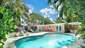 Un jardin avec une piscine, du mobilier de jardin et un petit bâtiment doté d’une porte et de fenêtres.