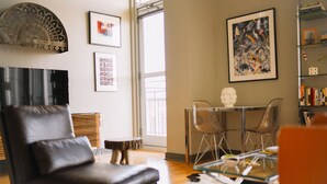 A modern living room with a leather chair, a glass coffee table, and a cowhide rug. There are framed pictures on the wall and a bust on a table.