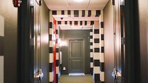 A hotel corridor with an exit sign, checkered walls, and a carpeted floor.