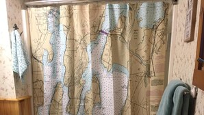 A bathroom with a map-themed shower curtain, wooden cabinets, and a blue towel hanging on the wall. - Year Round Lakeview Cottage with Dock on Lake Champlain (Alburg)