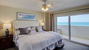 A bedroom with a large bed, a ceiling fan, a view of the ocean through a sliding door, and a framed picture on the wall. - Breathtaking Penthouse w/ Direct Oceanfront Views,  40' private balcony. (Daytona Beach Shores)