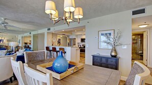 A spacious living room with a wooden dining table, a chandelier, and a large vase. - Breathtaking Penthouse w/ Direct Oceanfront Views,  40' private balcony. (Daytona Beach Shores)