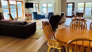 A spacious living room with a large window overlooking a scenic view, a dining area with wooden furniture, and a balcony with a view.
