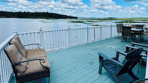 A deck with outdoor seating, a view of a lake, and a forested shoreline.