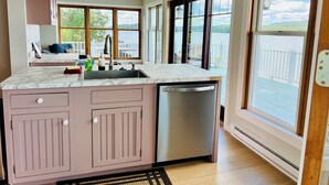A modern kitchen with a built-in dishwasher, a large window overlooking a lake, and a cozy seating area with a view.