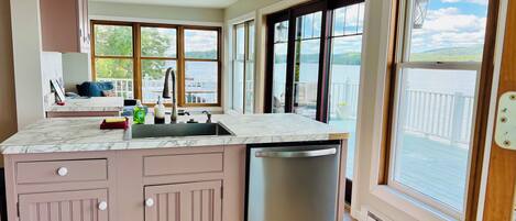 A modern kitchen with a built-in dishwasher, a large window overlooking a lake, and a cozy seating area with a view.