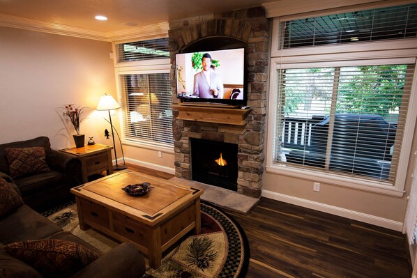 A living room with a stone fireplace, a television, and a cozy seating area with a coffee table and a lamp. - End of Summer Price Drop! Snowbasin Lakeside Luxury 3bd.Hot tub.Garage. 2300sqft (Huntsville)