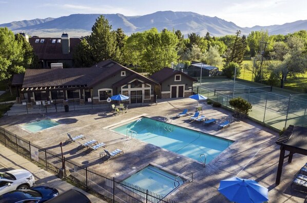 Ein Poolbereich mit zwei Pools, Liegestühlen, Sonnenschirmen und Blick auf Berge.