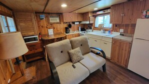 A compact RV kitchen with wooden cabinets, a stove, a sink, and a small seating area with a cushion.
