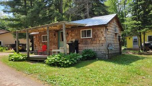 A rustic cabin with a porch, a small deck, and a covered outdoor area.