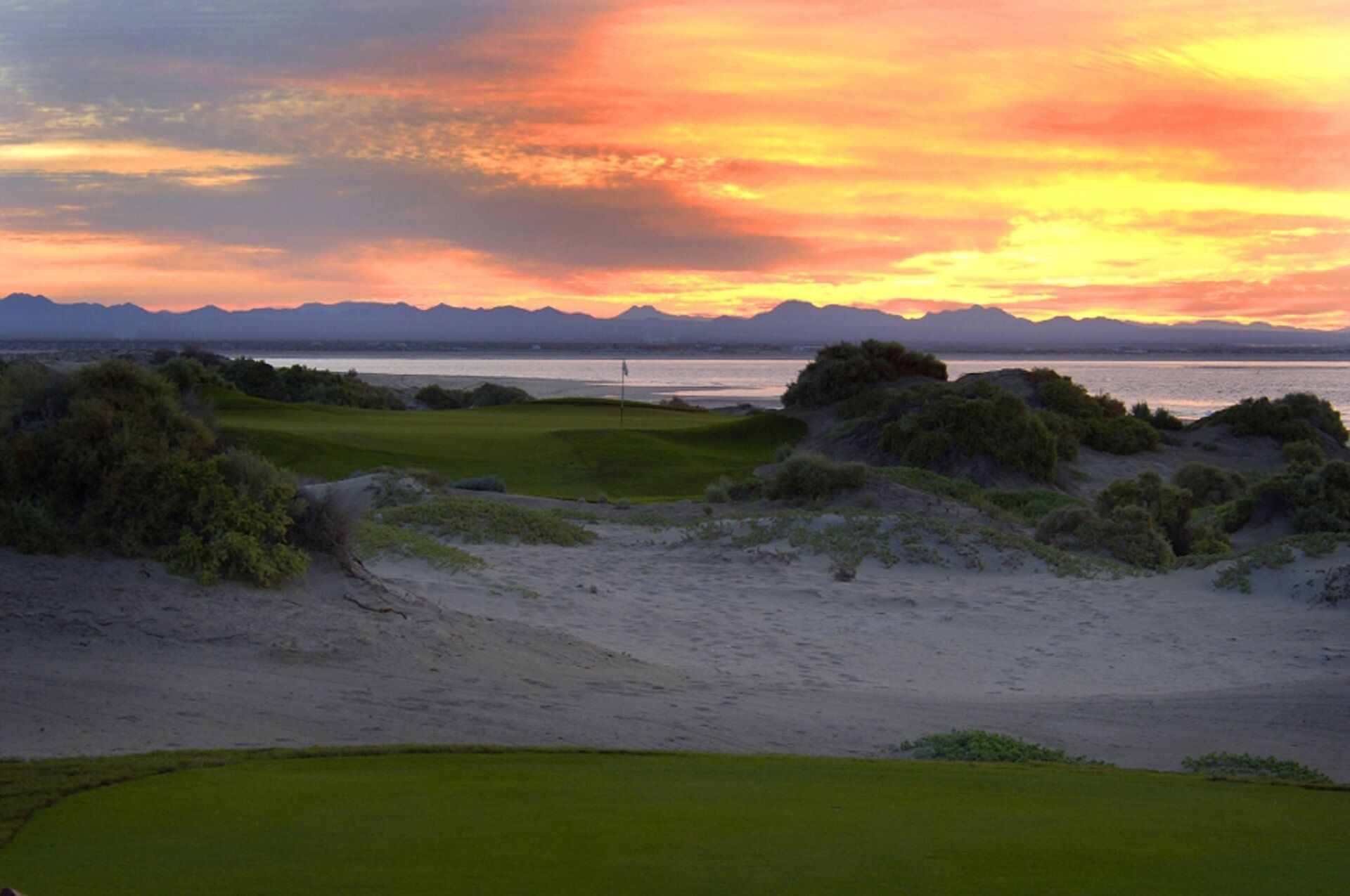 Un parcours de golf avec un mât de drapeau, des bunkers de sable et un plan d’eau en arrière-plan.