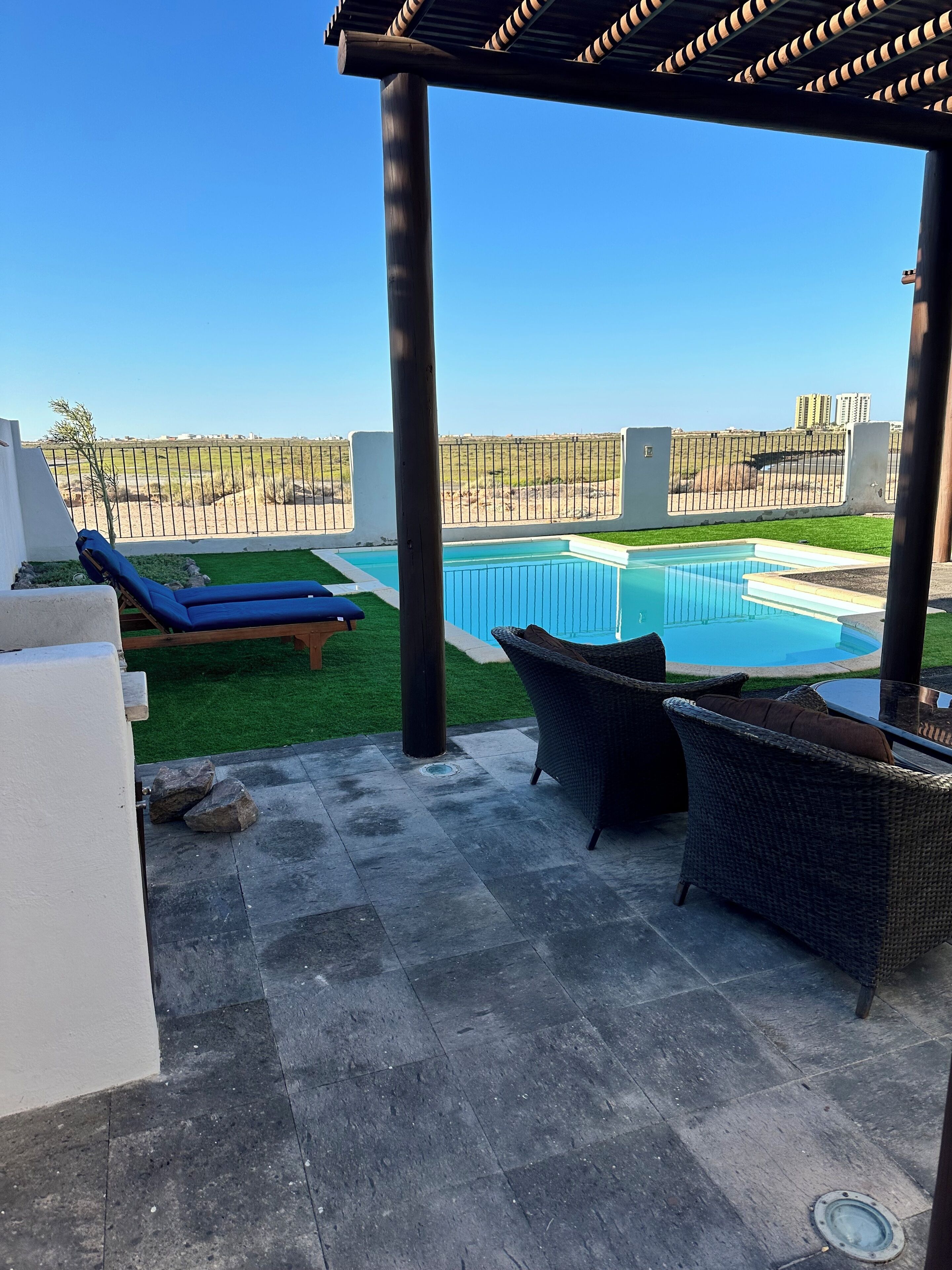 A covered outdoor area with a pool, lounge chairs, and a pergola.