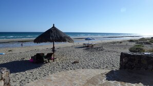 Een strand met een rieten parasol, stenen muren en enkele strandstoelen.