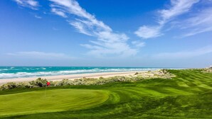 Een golfbaan met een vlag, uitzicht op de oceaan en een zandstrand.