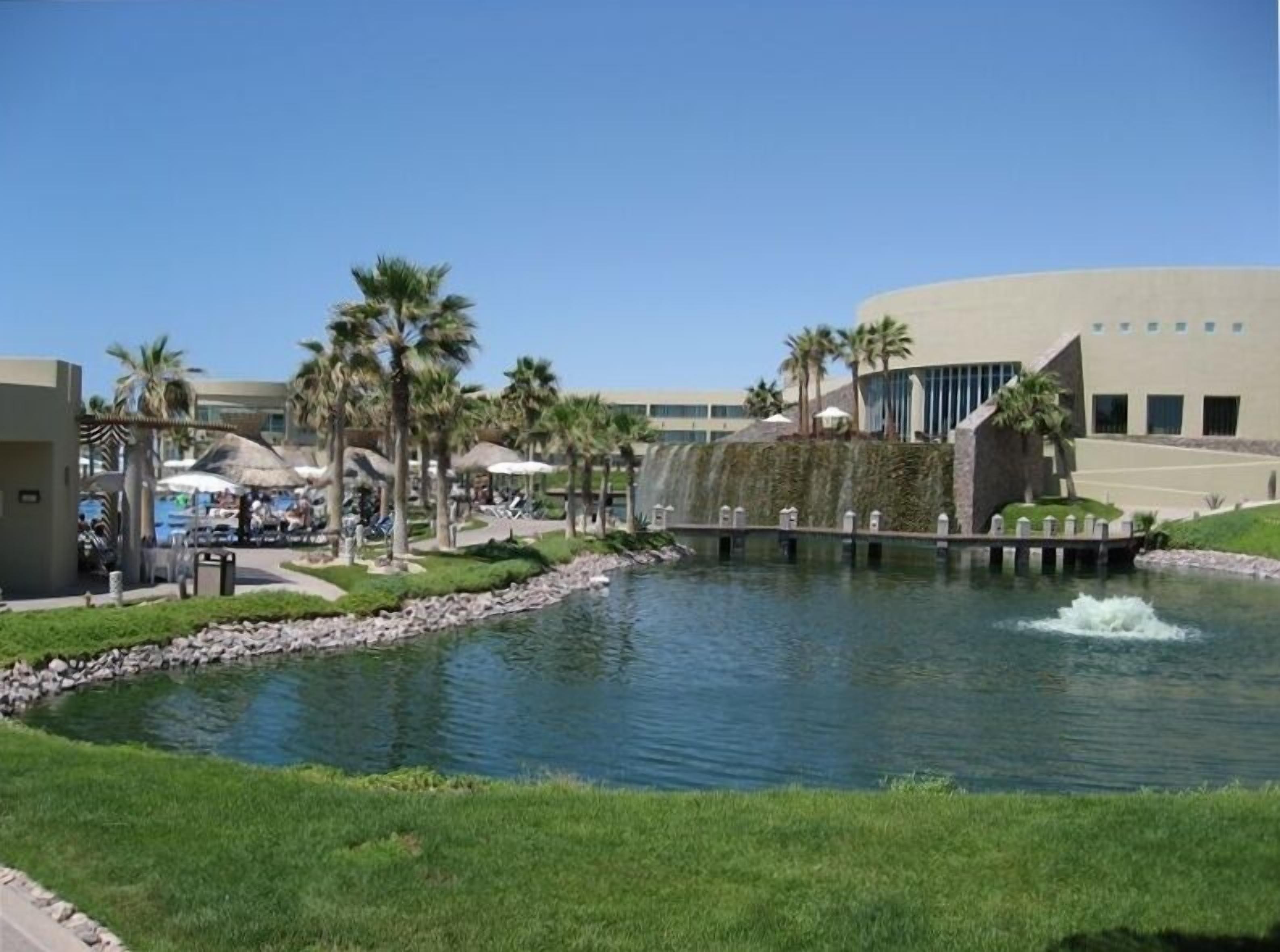 A resort with a swimming pool, palm trees, and a modern building with a curved facade.