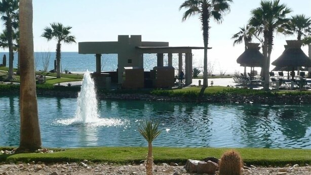 Een resort met een zwembad, palmbomen en een gebouw met een waterfontein.