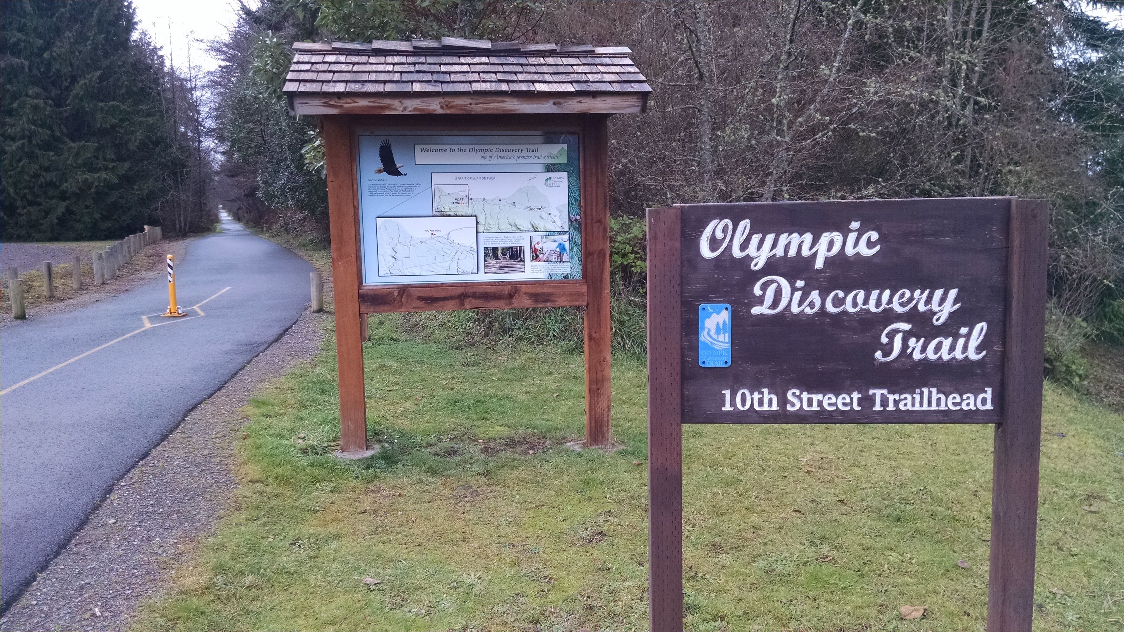 A wooden signboard with the text 'Olympic Discovery Trail 10th Street Trailhead' and a map.
