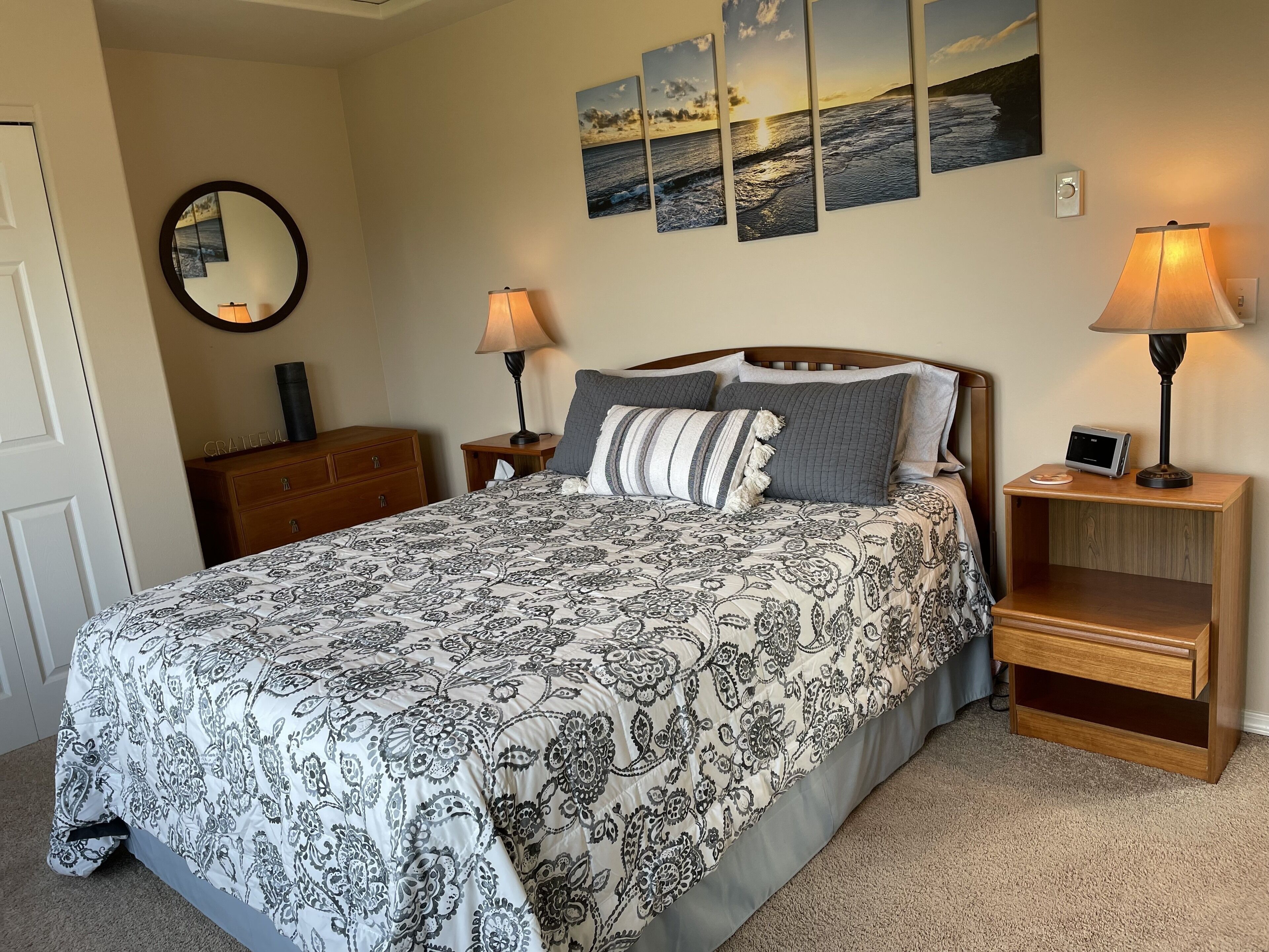 A neatly made bed with a patterned bedspread, two bedside lamps, a nightstand with a digital clock, and a wall-mounted mirror.