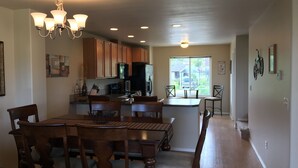 A spacious kitchen with wooden cabinets, a dining area with a chandelier, and a view through a large window. - Mountains to Sea Twin (Port Angeles)