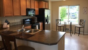 A kitchen with wooden cabinets, a black refrigerator, a microwave, and a stove. There is a sink with a faucet, a chair, and a table with chairs. - Mountains to Sea Twin (Port Angeles)