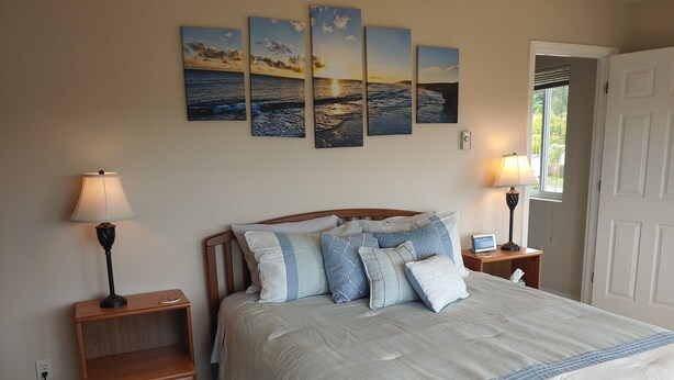 A bedroom with a bed, two bedside tables, a lamp, a wall-mounted picture, and a door. - Mountains to Sea Twin (Port Angeles)