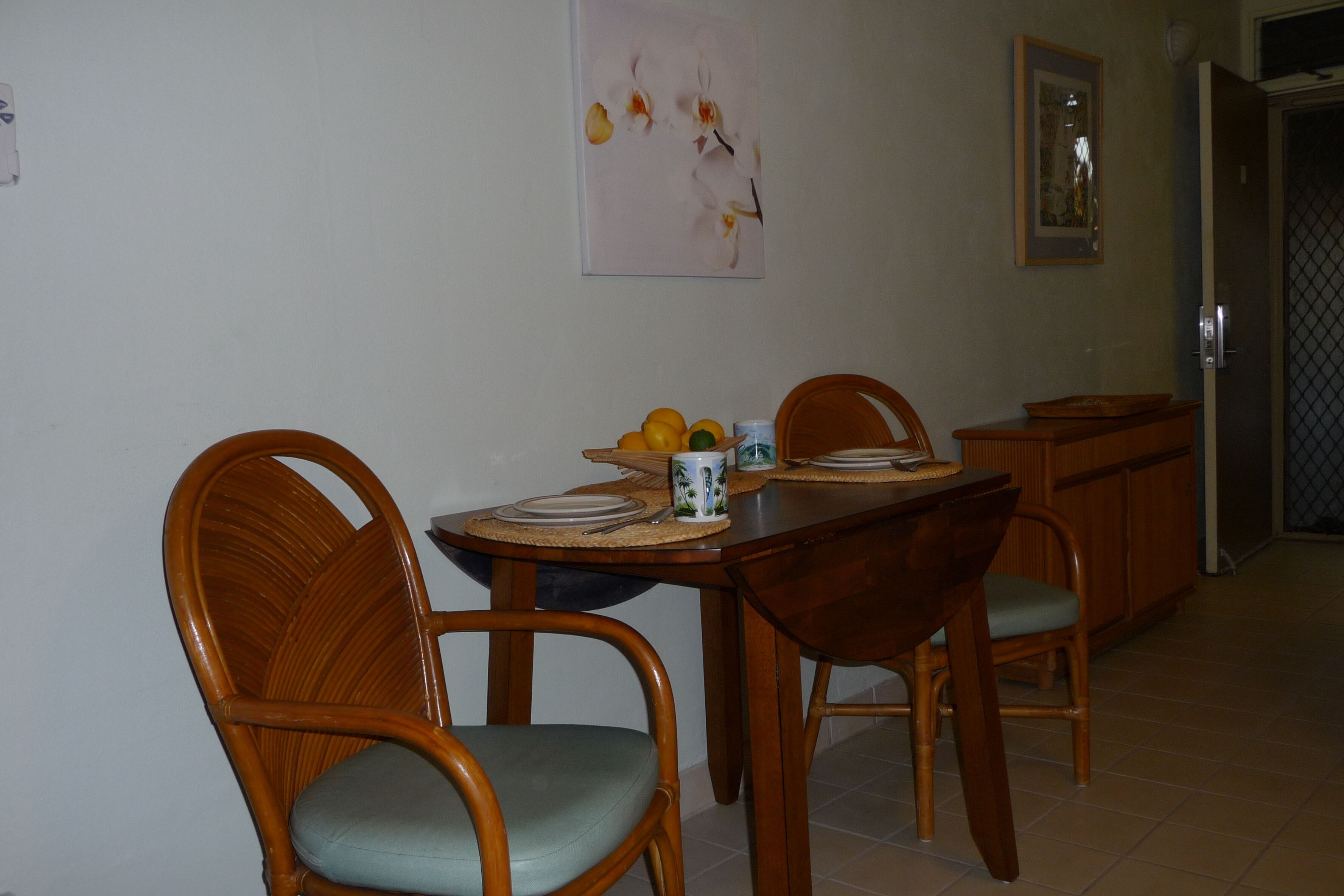 A dining area with a wooden table and chairs, a fruit bowl, and a framed picture on the wall.