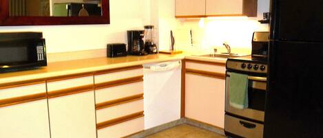 A compact kitchen with a microwave, coffee maker, toaster, and a refrigerator.