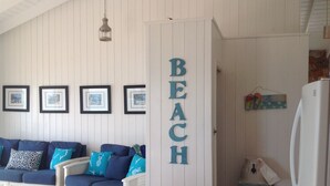 Ein Zimmer mit weißer Wand, einem blauen Sofa mit gemusterten Kissen, einer Bildergalerie und einem Schild mit der Aufschrift 'BEACH'.