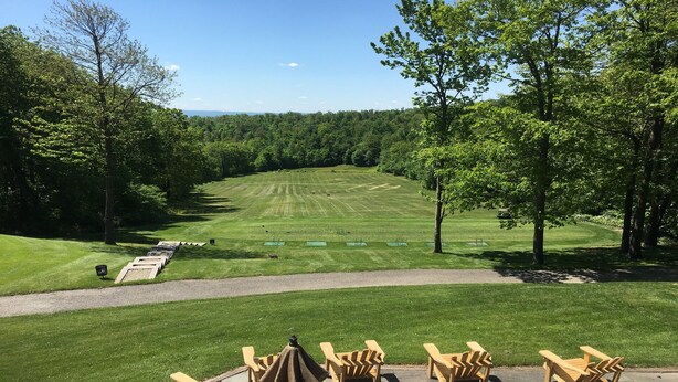 A golf course with a clear view of the fairway, sand bunkers, and a flagstick. There are wooden chairs and a tent set up for viewing.