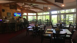 A restaurant with wooden beams, a bar area, and large windows offering a view of trees.