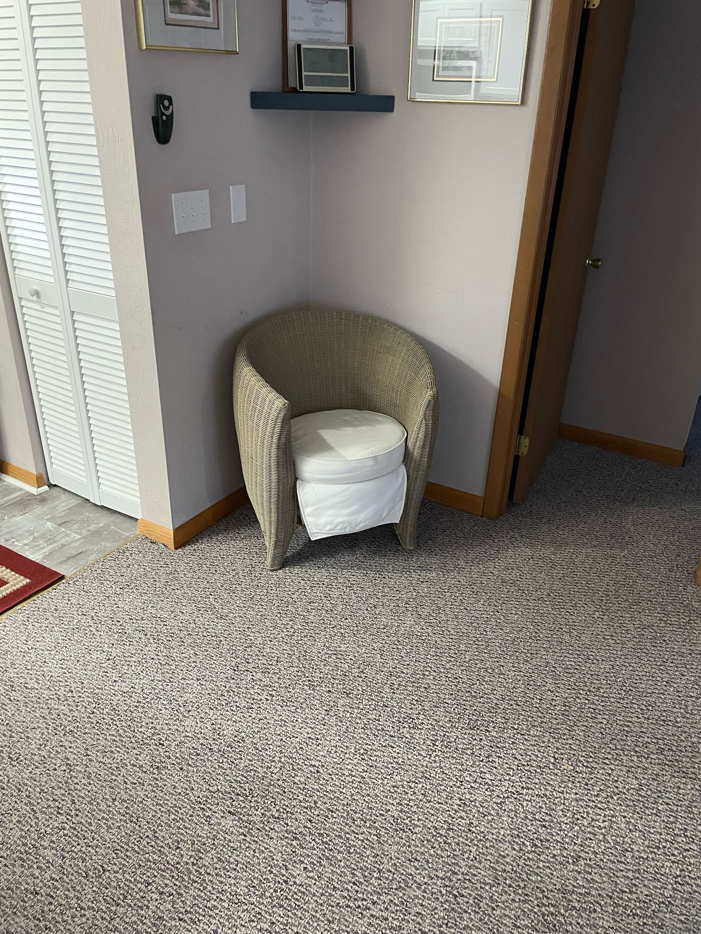 Une pièce d’angle avec un fauteuil en osier, un petit tapis et une porte.