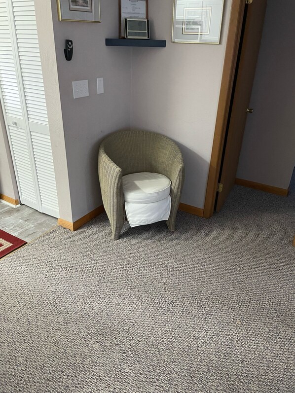 Una habitación de esquina con una silla de mimbre, una alfombra pequeña y una puerta.