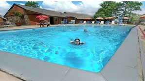 A swimming pool with lounge chairs and umbrellas, a wooden building, and a clear sky.