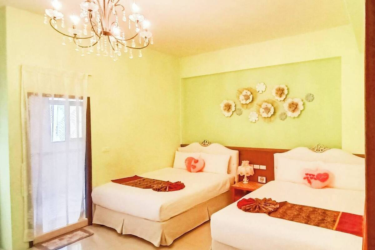 A hotel room with two beds, a chandelier, a wall with decorative plates, and a window with curtains.