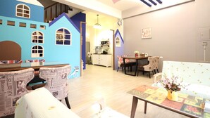 Un área de juegos infantiles con una casita azul, una mesa de comedor con sillas y un sofá.