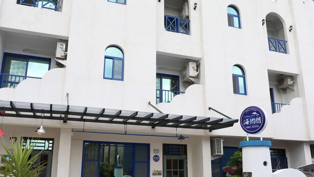 Un edificio de varios pisos con fachada blanca y detalles azules, que cuenta con una entrada cubierta y un cartel que indica un restaurante.