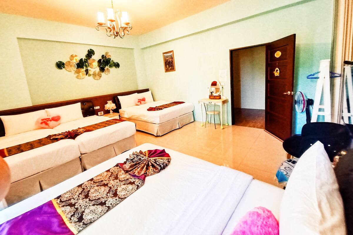 A hotel room with a large bed, a sofa, a desk with a chair, and a chandelier.