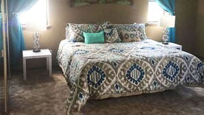 Ein Schlafzimmer mit einem gemusterten Bett, einem kleinen Nachttisch mit einer Lampe und einem Deckenventilator.