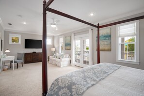 A spacious bedroom with a large bed, a ceiling fan, a desk, and a view of the outdoors through a sliding glass door.