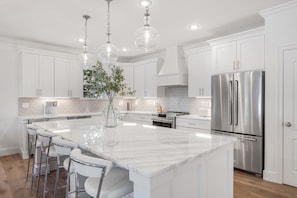 A modern kitchen with white cabinetry, a large marble island, stainless steel appliances, and pendant lighting.