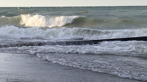 Une plage où les vagues s’écrasent contre une barrière en béton.