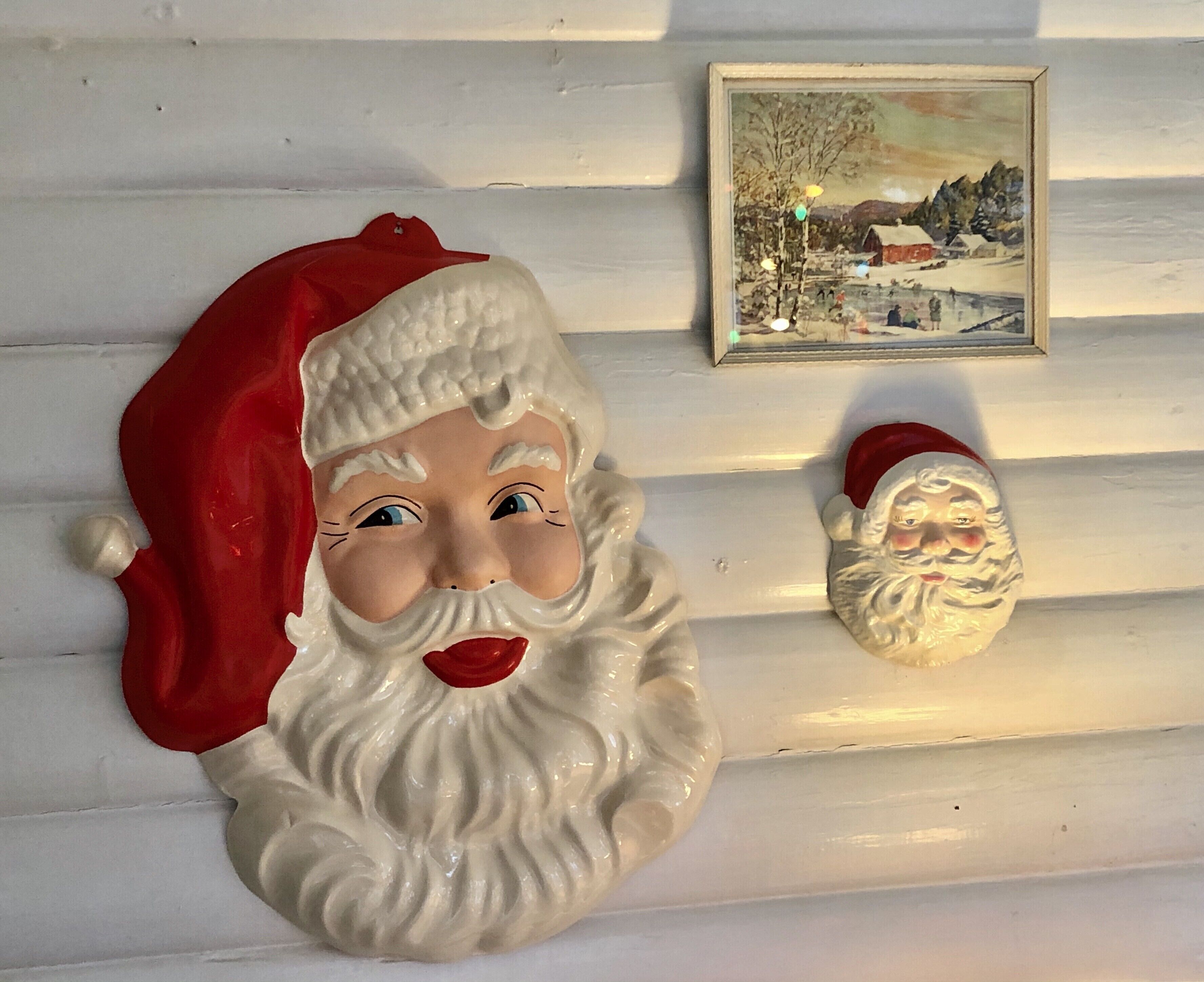 Kaksi Joulupukin kuvaa koristamassa valkoista paneeliseinää.